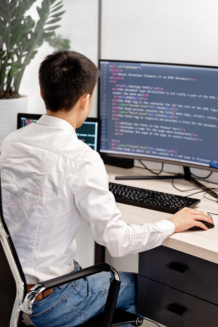 Back view of a programmer in a white shirt coding in an office workspace.
